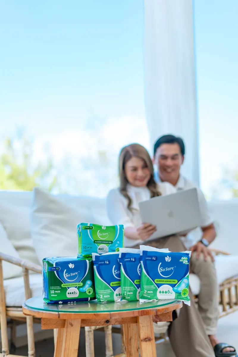 A relaxed couple share a laptop while the full So Sure pad range sits on a table in front of them.