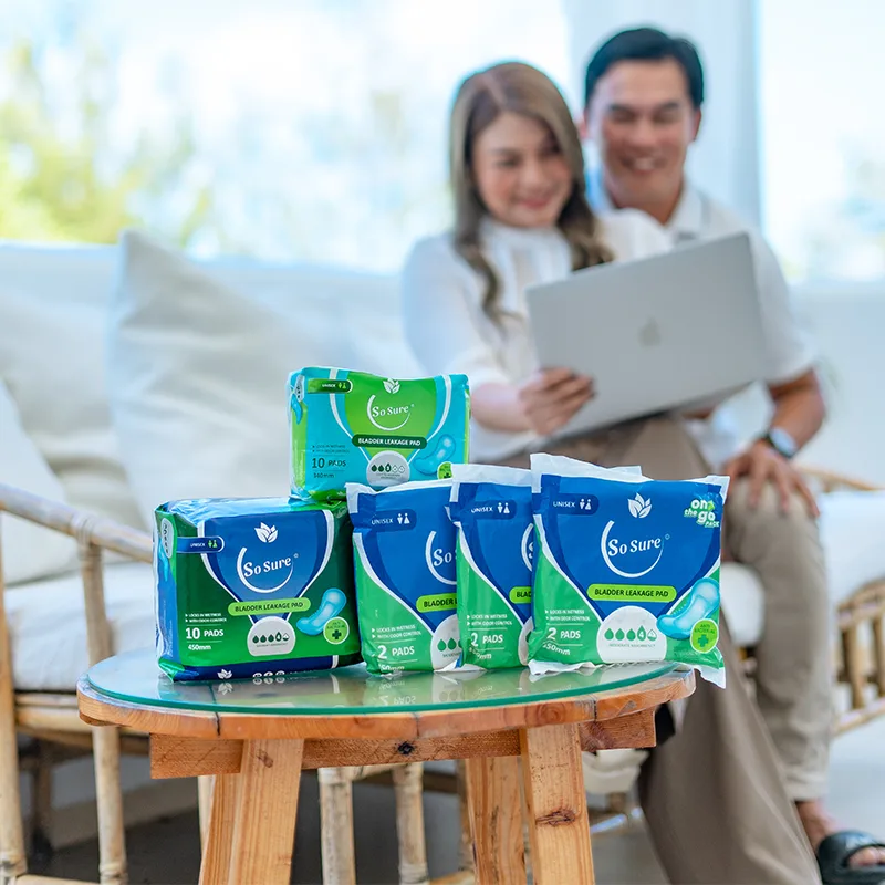 A relaxed couple share a laptop while the full So Sure pad range sits on a table in front of them.