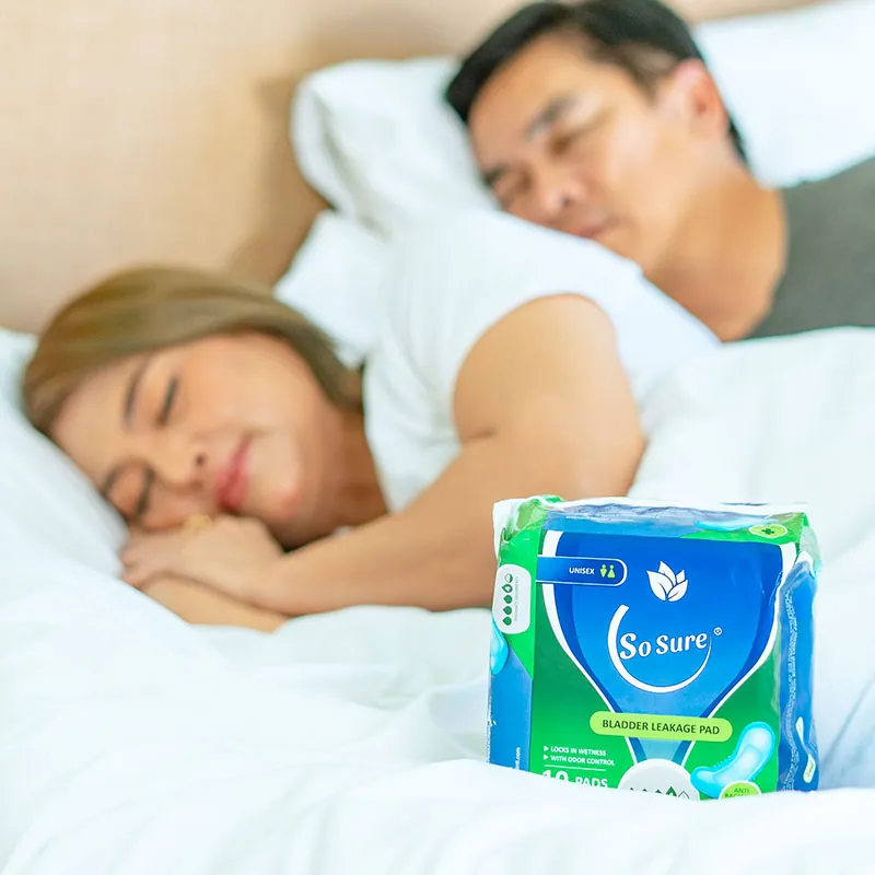 A couple sleep peacefully in bed with a So Sure bladder leakage pad pack resting in the foreground.