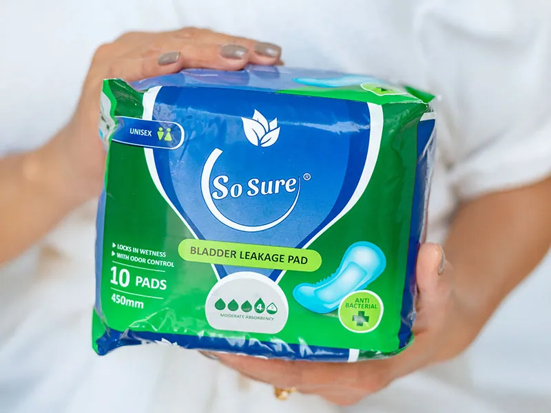 A woman holds a So Sure 450mm bladder leakage pad pack in both hands.